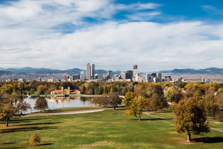 Denver skyline in autumn daylight. Mountains are visible in the background with a fresh sparsely cloudy sky.